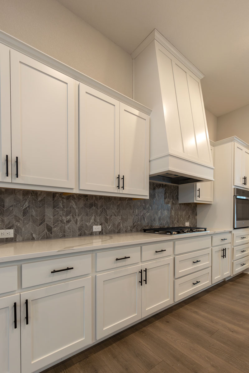White kitchen cabinets with Shaker cabinet doors in OE4, IE2, flat panel with custom wood vent hood and black hardware